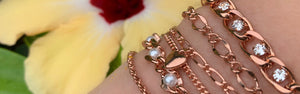 model wearing a variety of rose gold bracelets from Inch of Gold with hibiscus in the background